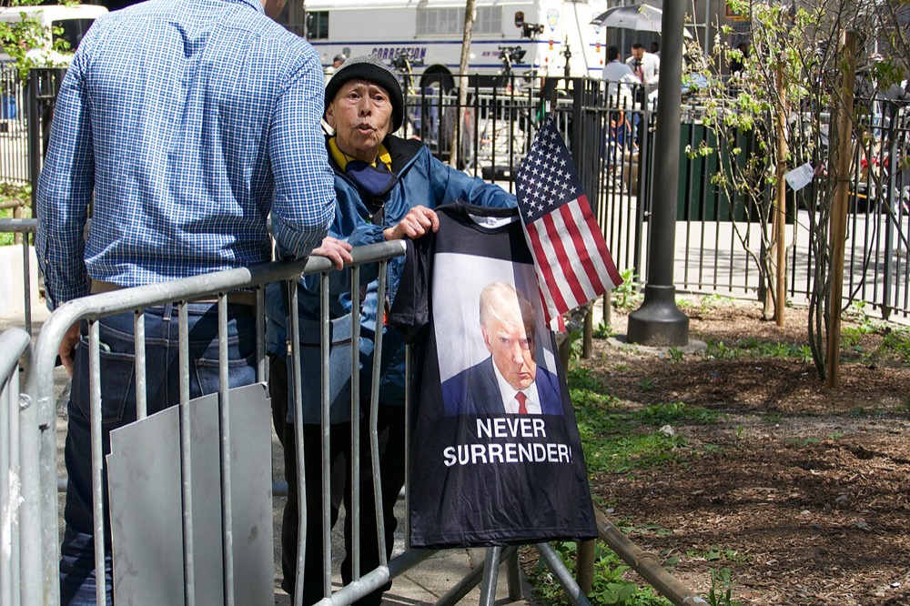 A supporter outside the Manhattan criminal court during Trump's 2024 trial, holding a Never Surrender shirt printed with his mug shot